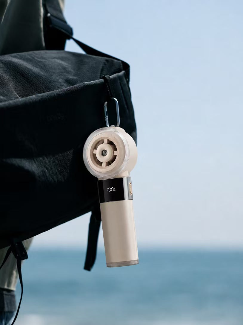 COOLIVA digital handheld fan clipped to a black bag by the sea